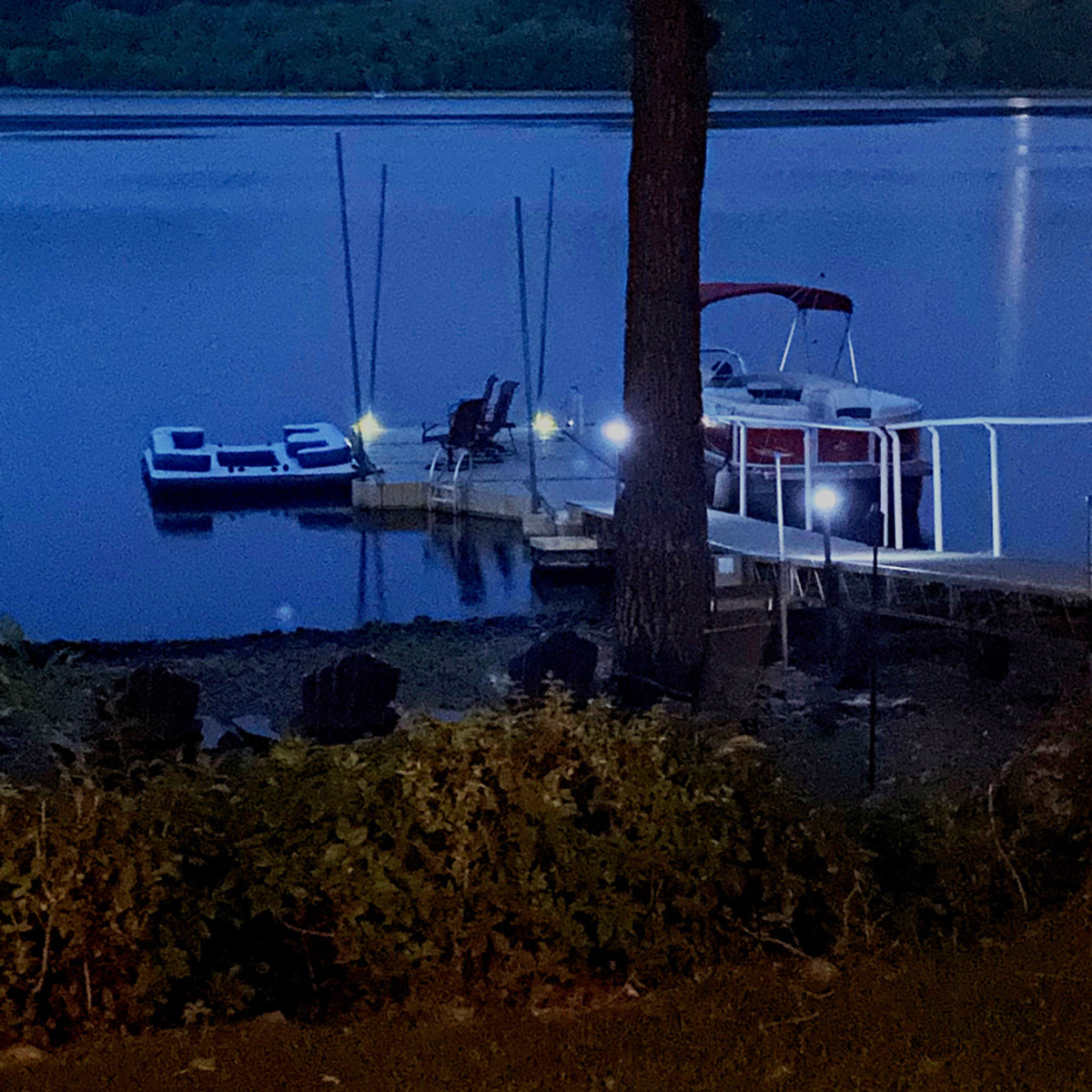 Boats docked at a pier on a lake at night with lights illuminating the scene.
