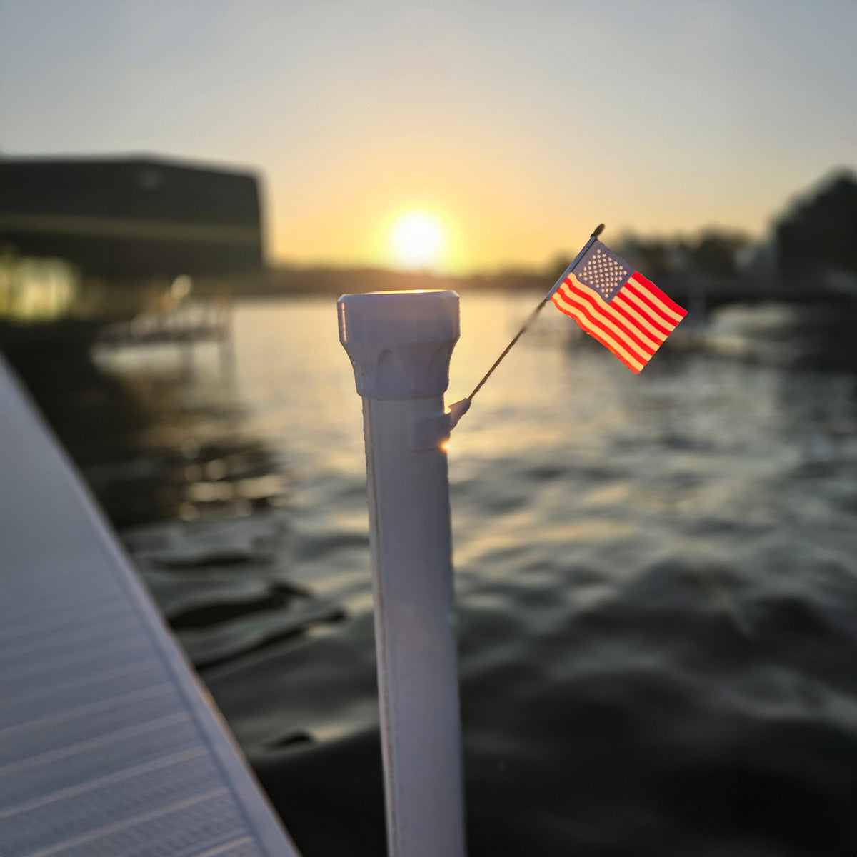American flag on a pole with a sunset over water in the background