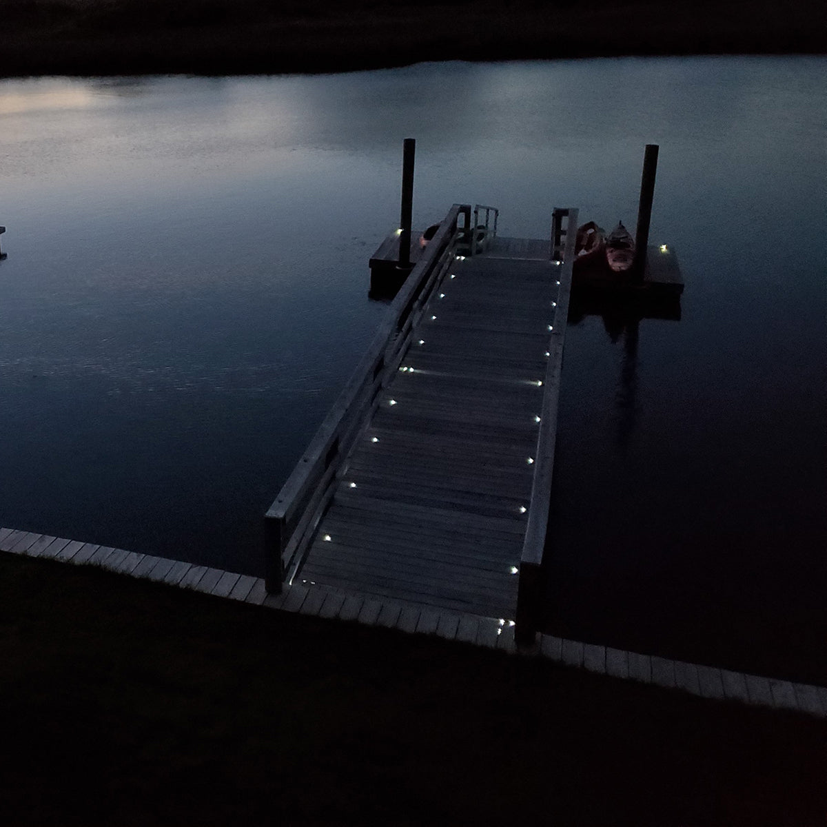 Wooden dock extending into a calm lake at night with lights on