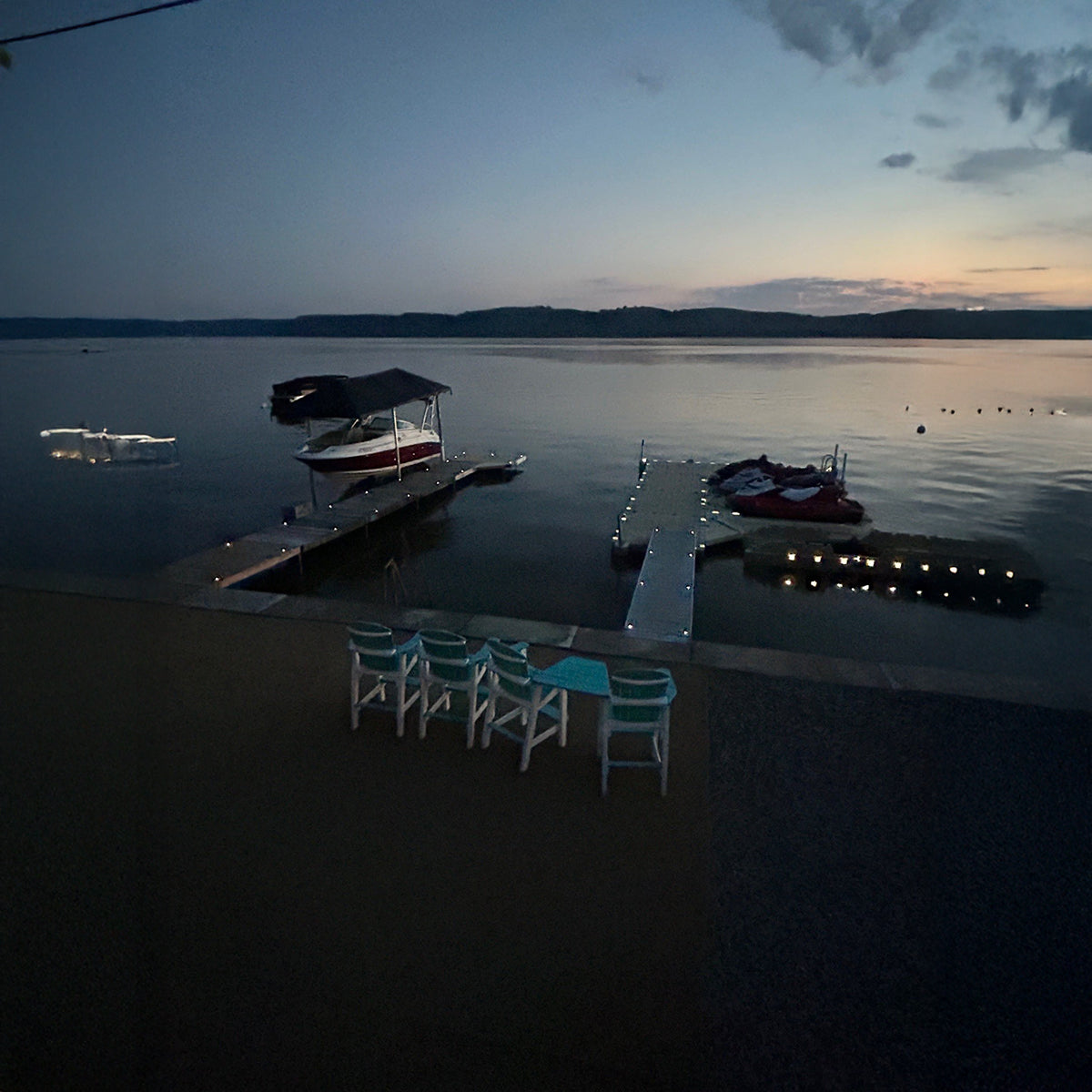 Evening scene at a dock with boats and chairs on a lake.