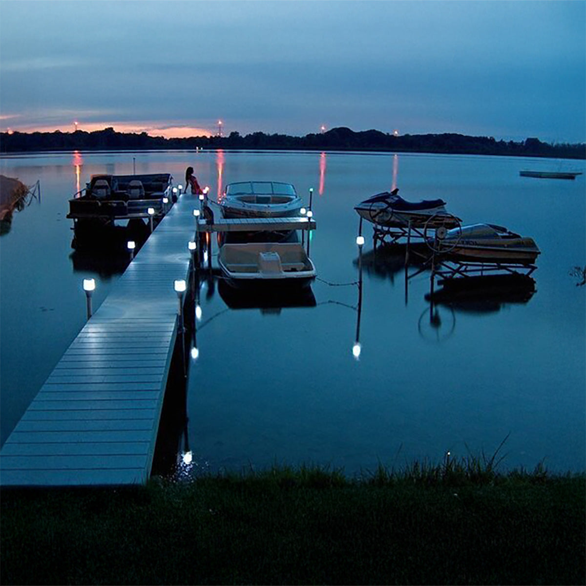 Evening scene at a dock with boats and lights reflecting on water