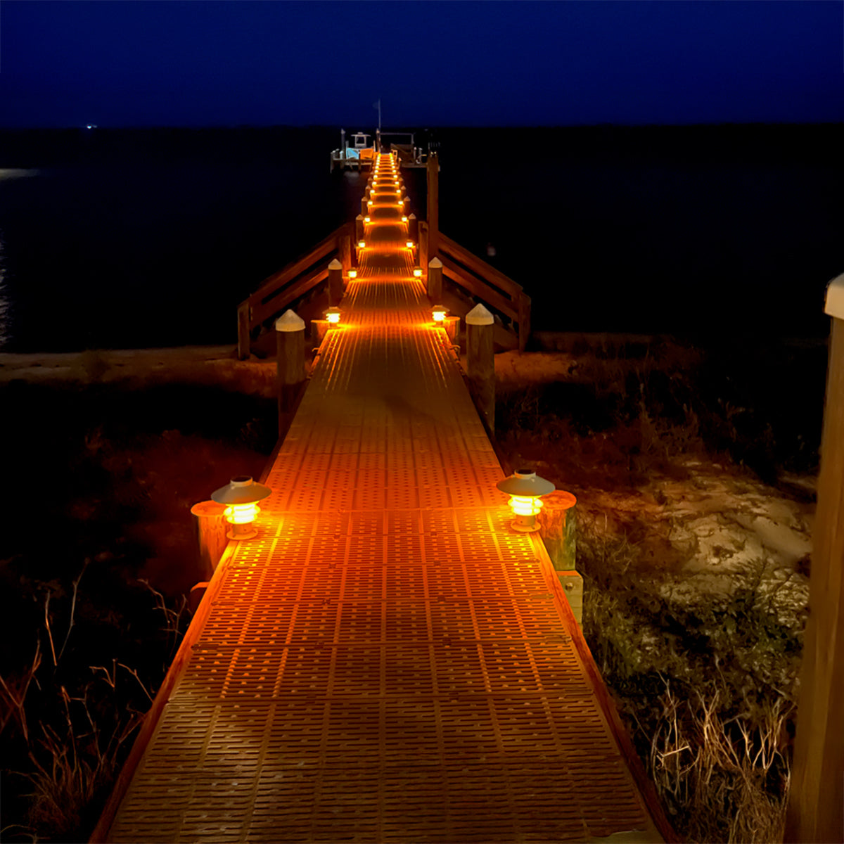 Wooden pier extending into the night with glowing lights on a dark background