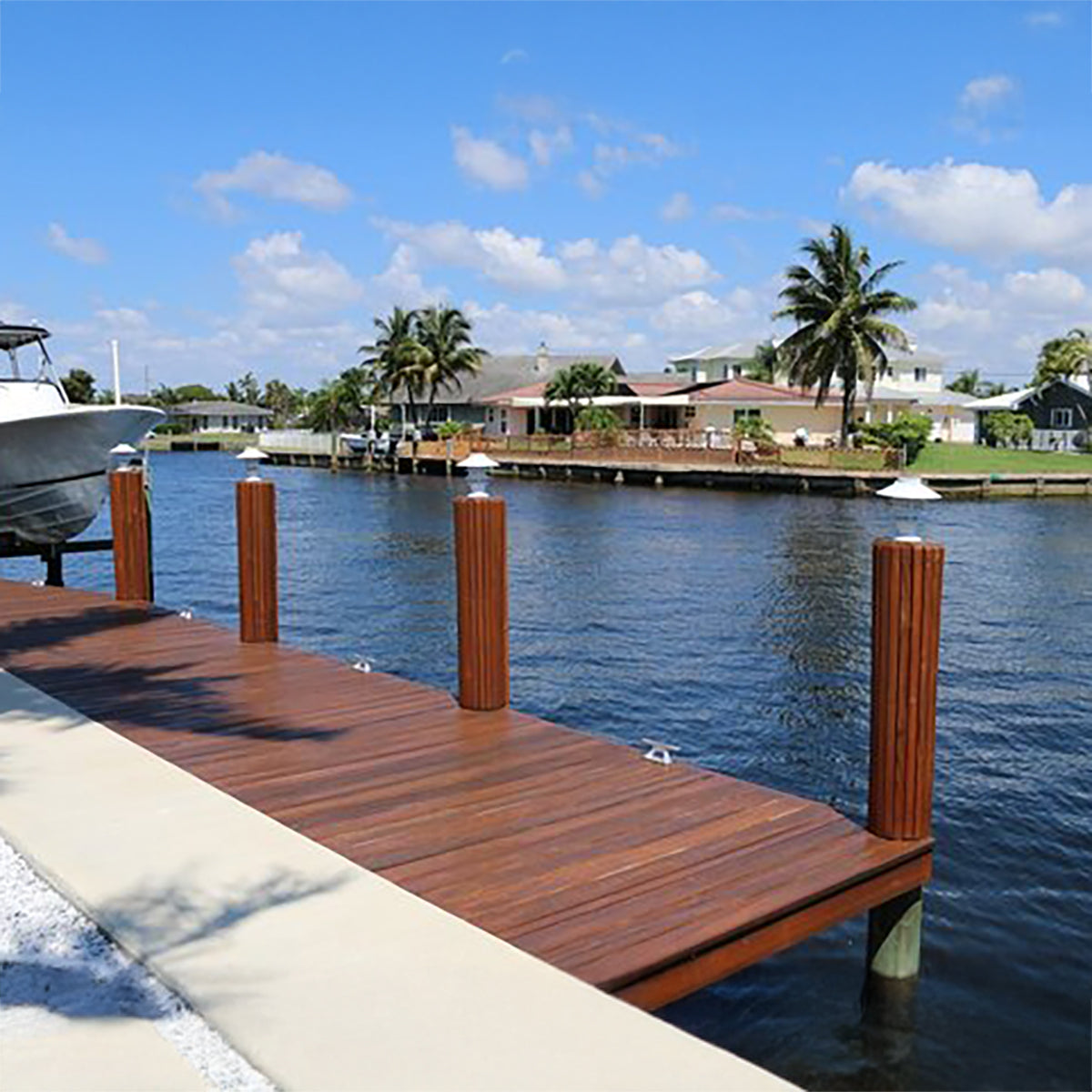 Wooden dock extending into a body of water with palm trees and houses in the background.
