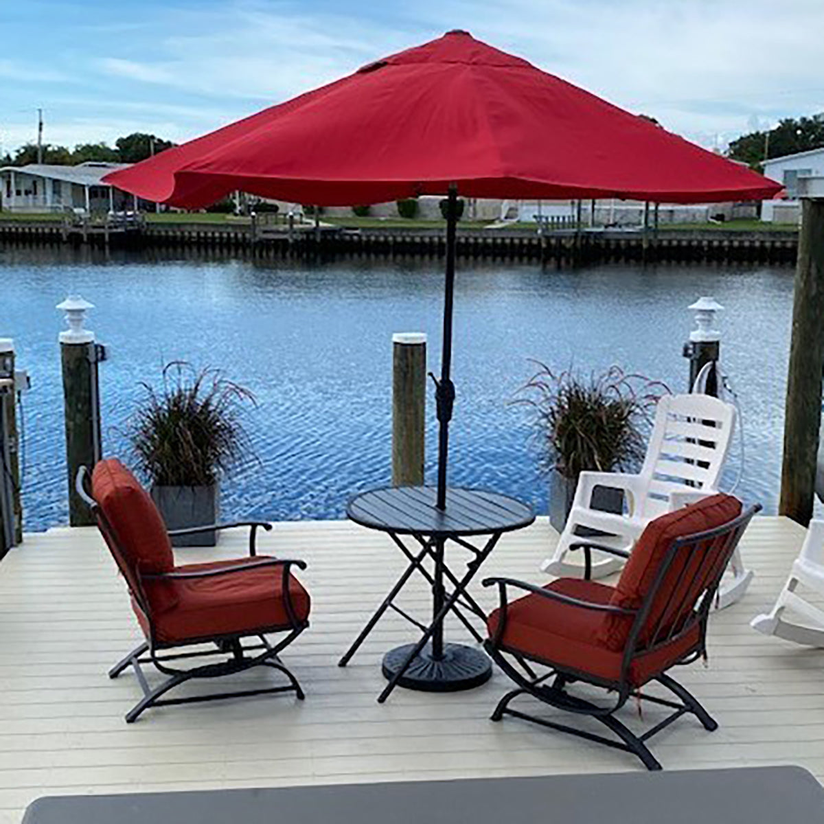 Outdoor patio set with red chairs, table, and umbrella by a waterfront.