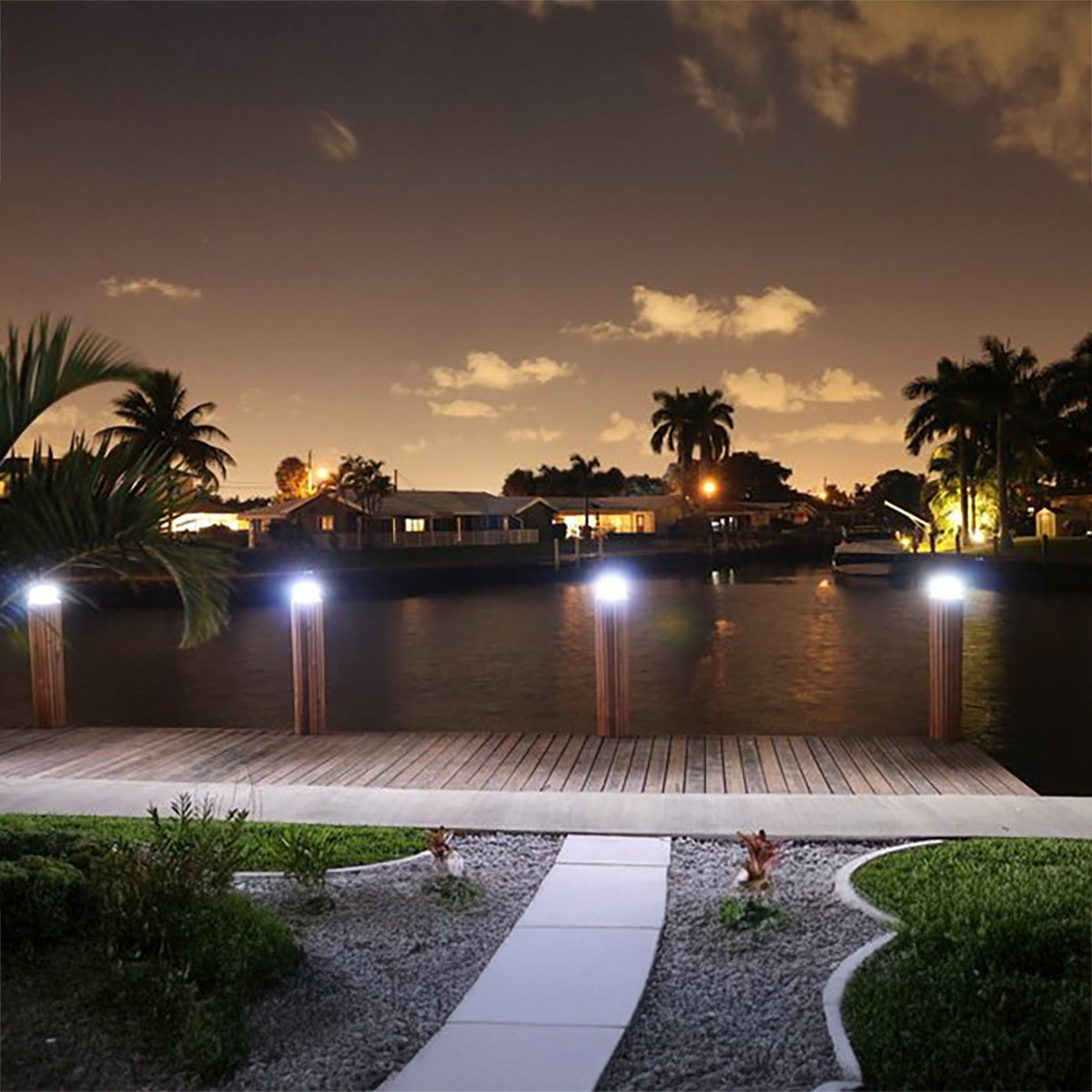 Evening view of a waterfront property with dock lights and palm trees.