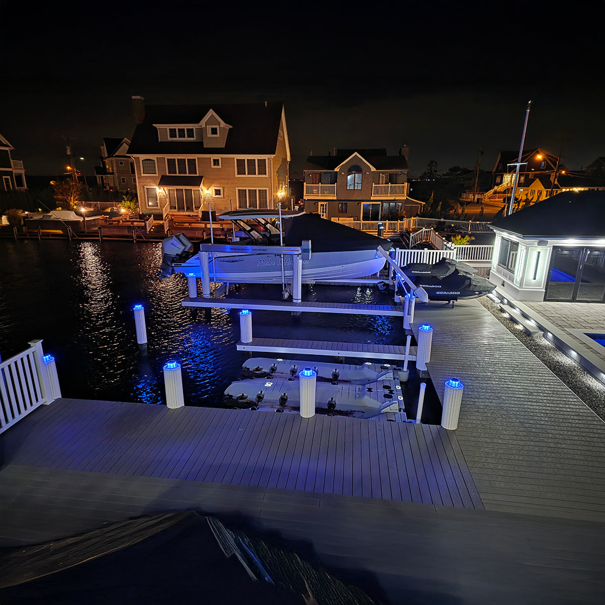 Dock with illuminated lights at night, waterfront houses in the background