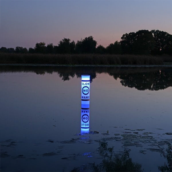 illuminated buoy floating on water at dusk with trees in the background