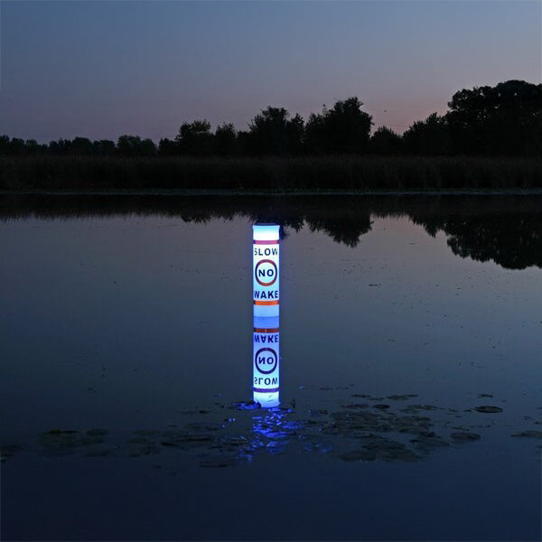 Floating light pole with warning signs on a body of water at night
