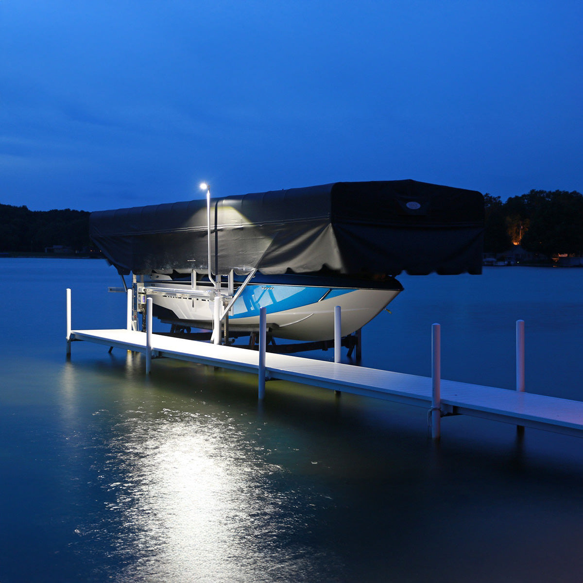 Boat on a dock under a black cover at night with a light illuminating the scene.