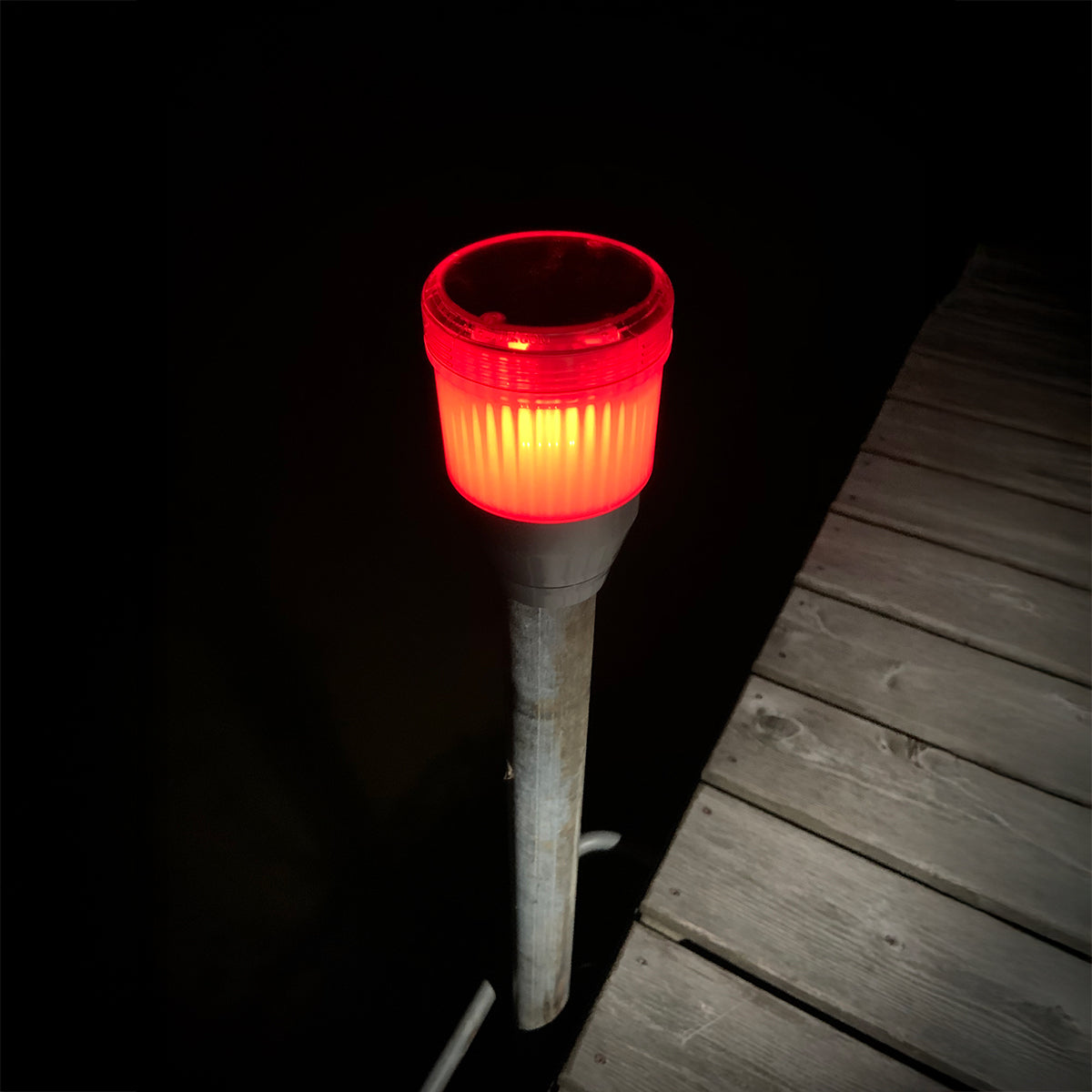 Red light on a metal pole on a wooden deck at night