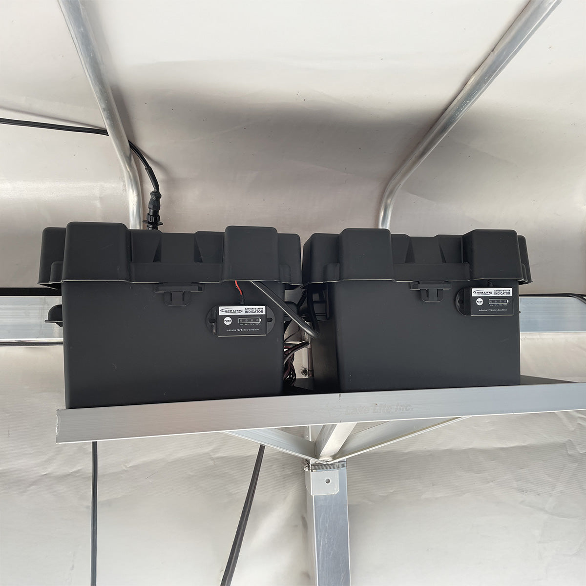 black battery boxes mounted on a metal shelf inside a boat canopy