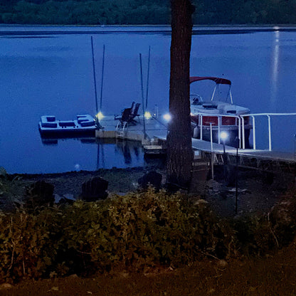 Boats docked at a pier on a lake at night with lights illuminating the scene.