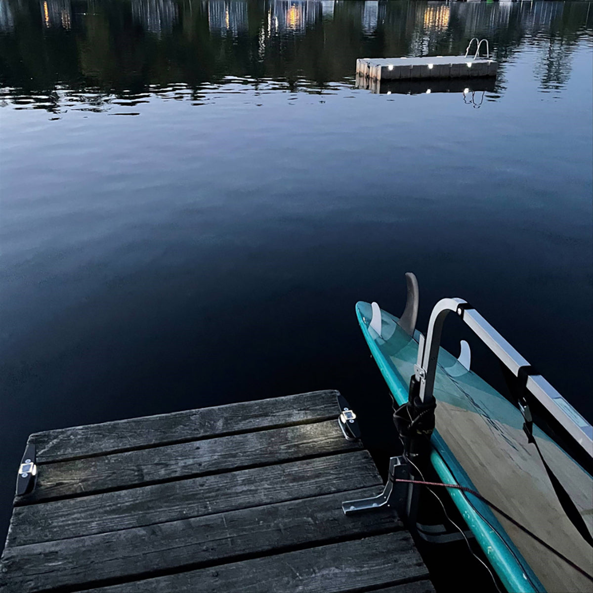 Teal kayak tied to a wooden dock with calm water and another dock in the background.