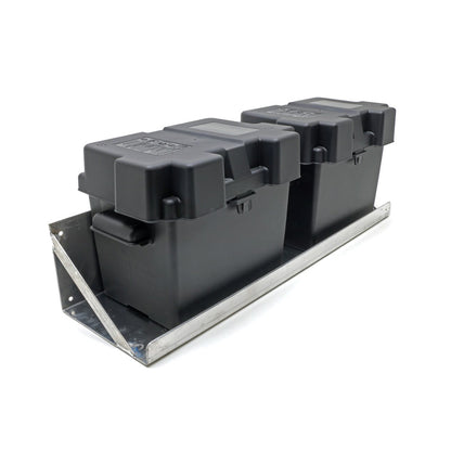 2 black plastic battery boxes sitting on a wall mounted dual battery tray. 