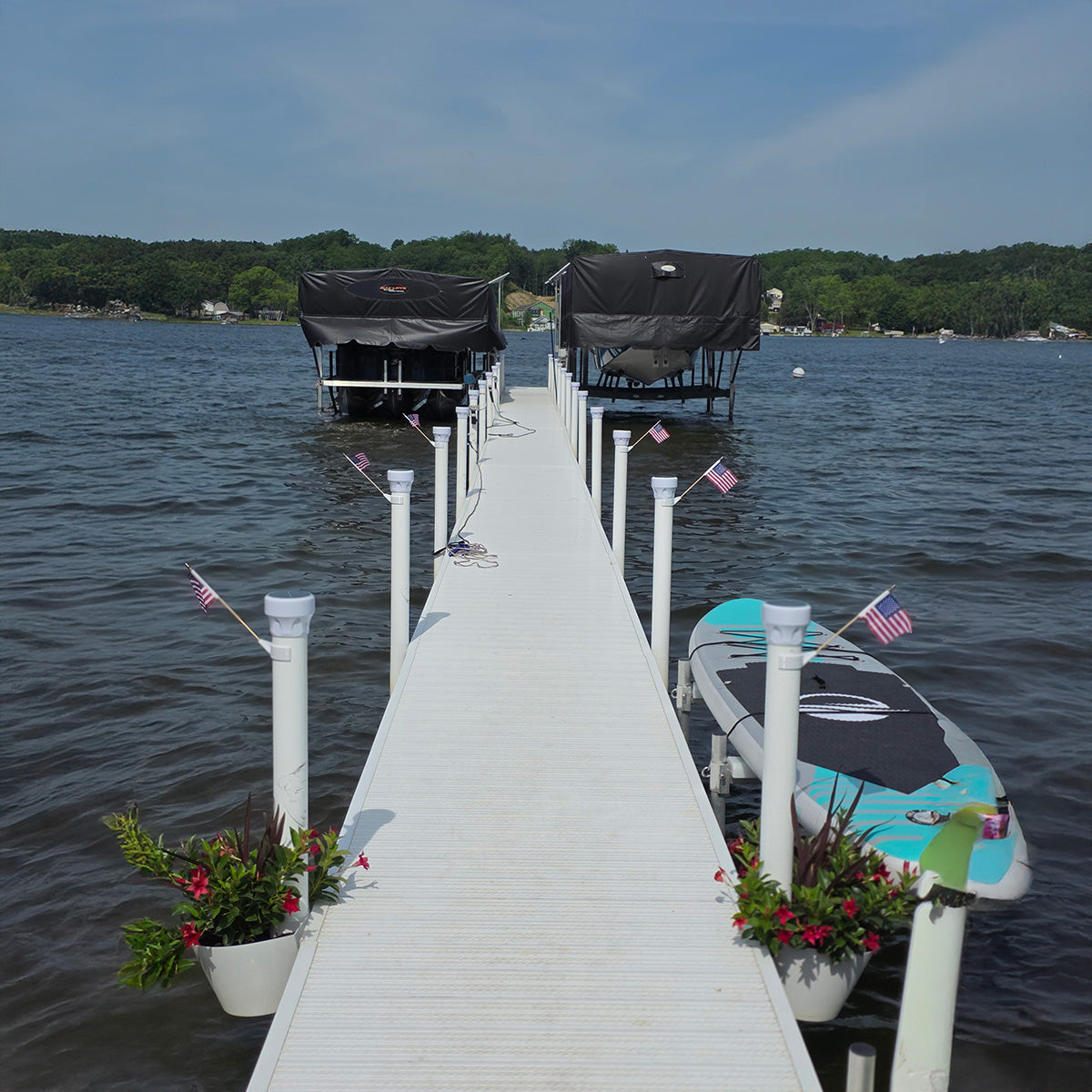 White dock extending into a body of water with boats and flags.