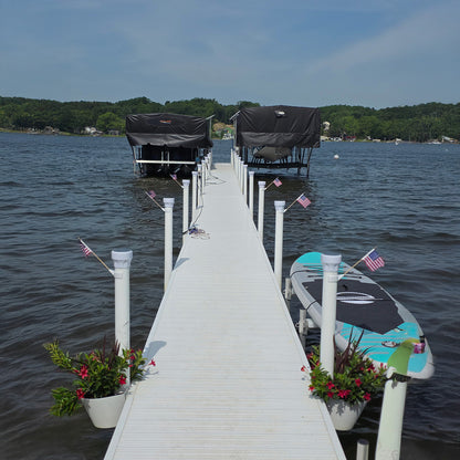 White dock extending into a body of water with boats and flags.