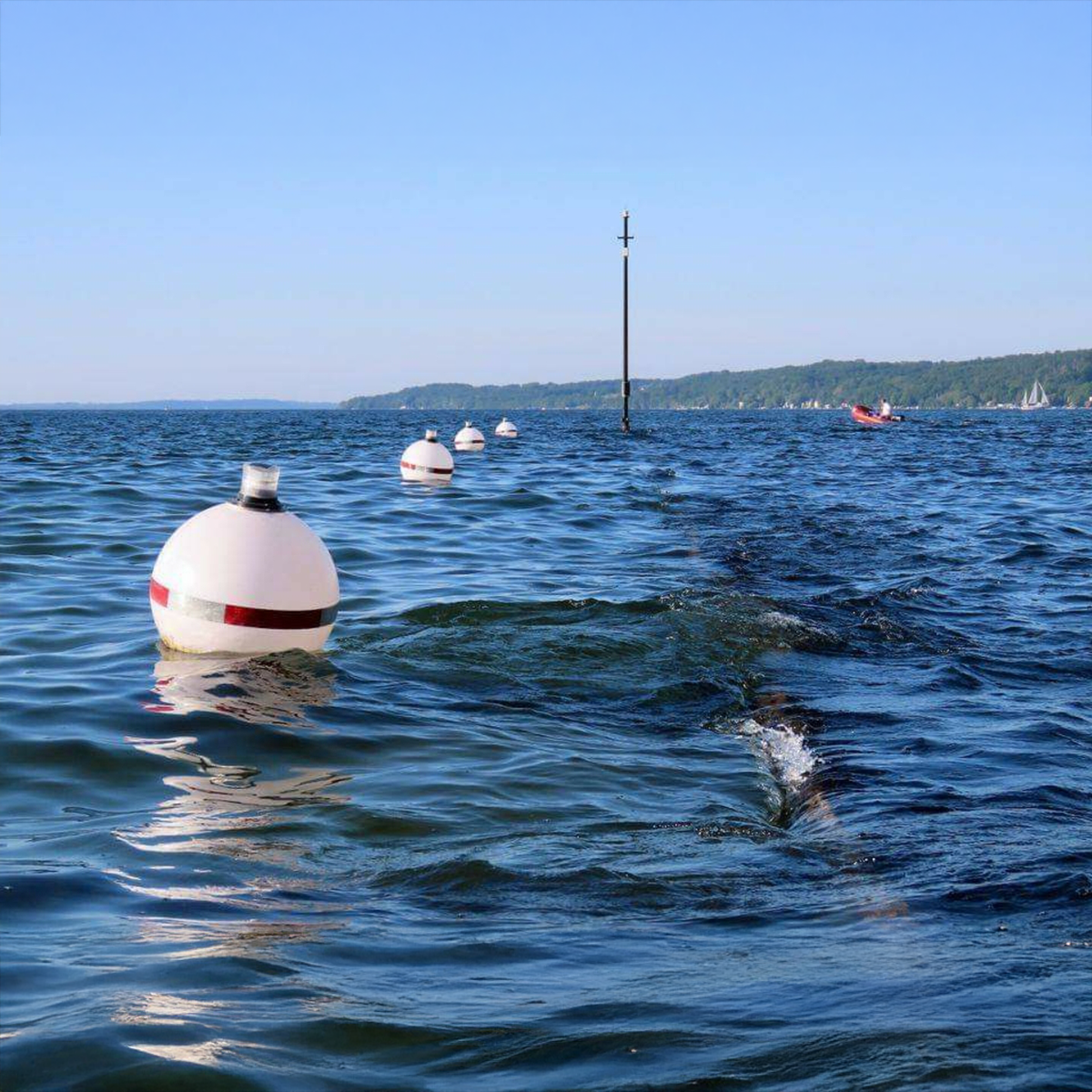 Buoy floating in the water with a clear blue sky and distant shoreline.