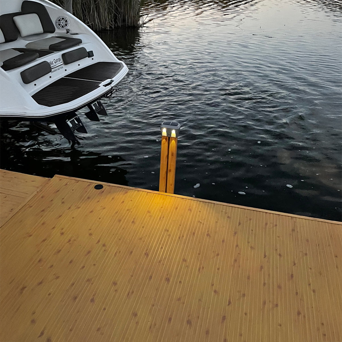 White boat on water near a wooden dock with two lights.