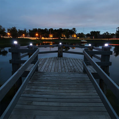 Wooden dock extending over a body of water at night with lights illuminating the area.