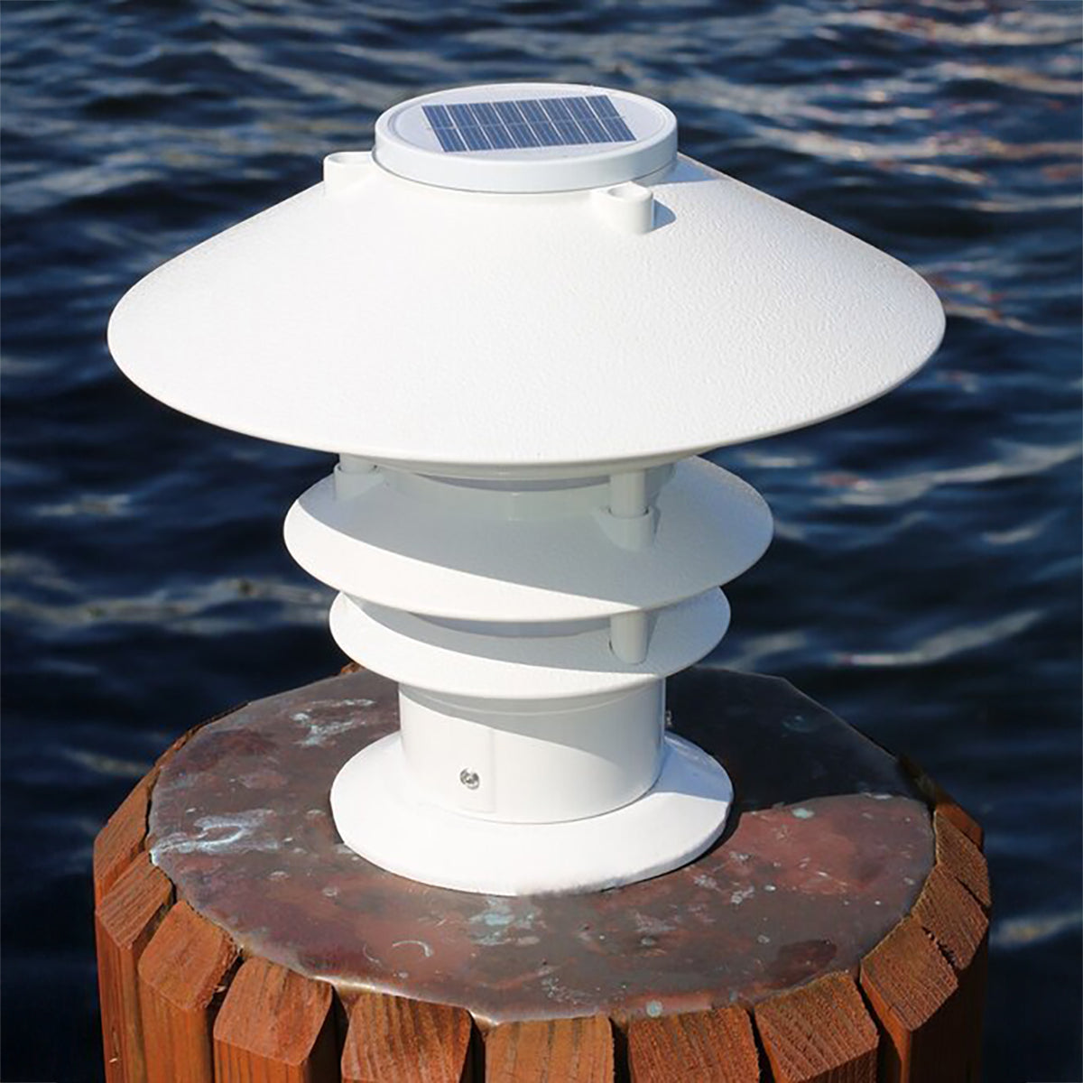 White solar light fixture on a wooden post with water in the background