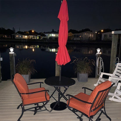 Outdoor patio set with orange chairs, black table, and red umbrella on a dock at night.