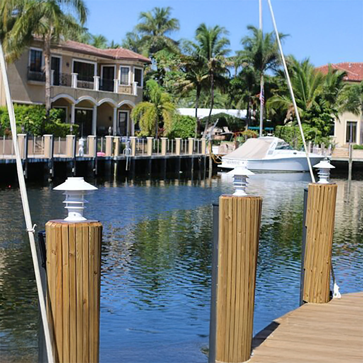Marina scene with wooden dock posts, house, and boat under a clear blue sky.