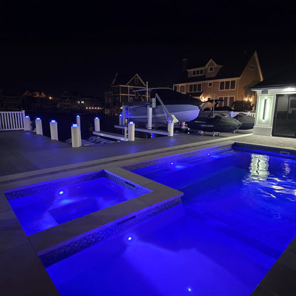 Pool area with illuminated hot tub and boats at night
