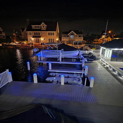 Dock with illuminated lights at night, waterfront houses in the background