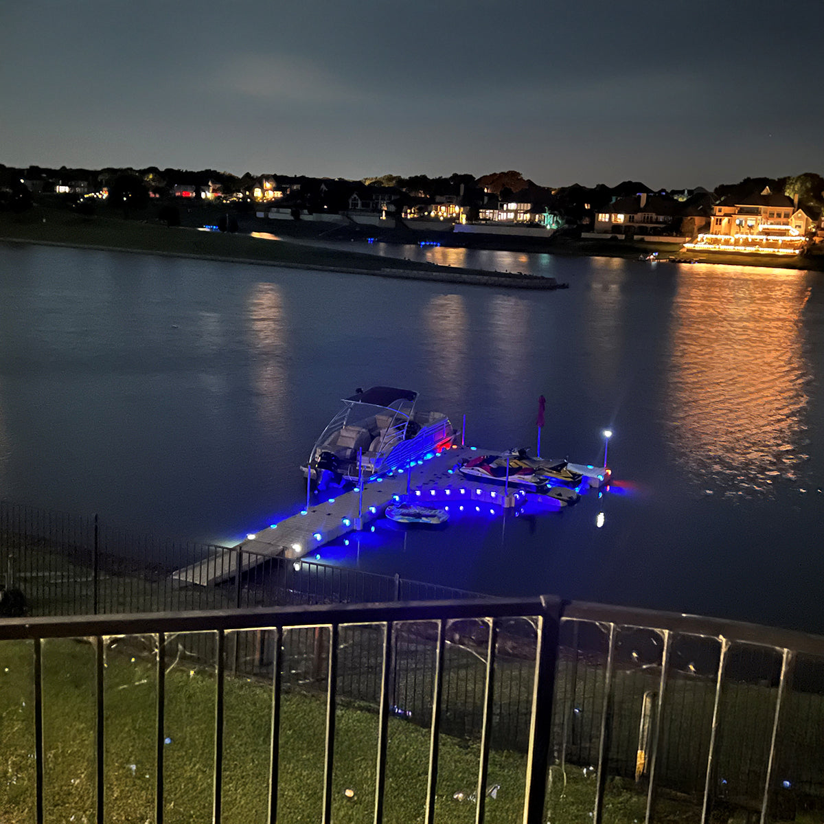 Boat docked at a marina with blue lights at night, surrounded by water and distant lights.