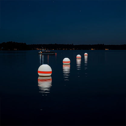 Three illuminated buoys on a calm lake at night with a dark sky.