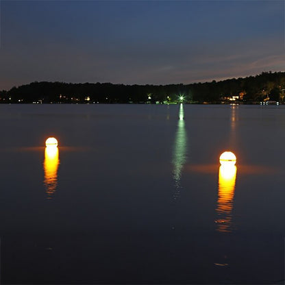 Two illuminated buoys on a calm lake at night with trees in the background.