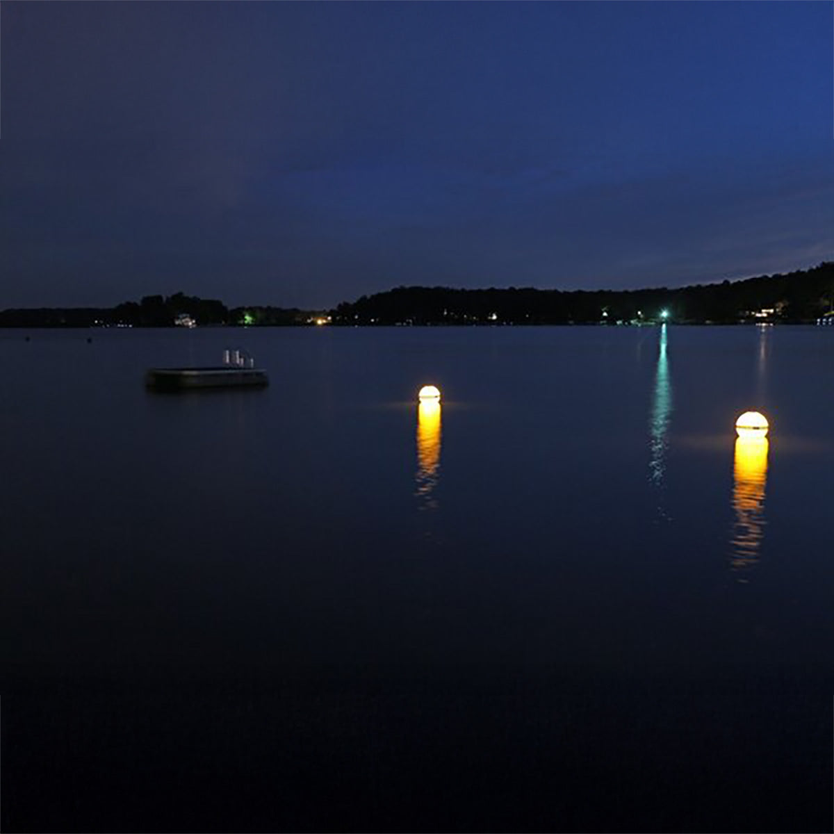 Two illuminated lanterns floating on a calm lake at night.