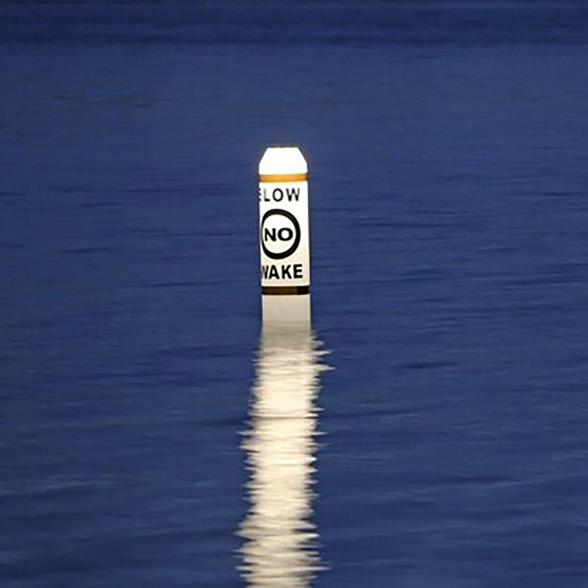 Floating buoy with 'LOW NO WAKE' sign on a calm blue water surface