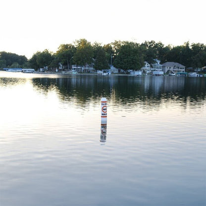 Buoy floating in a calm lake with houses and trees in the background