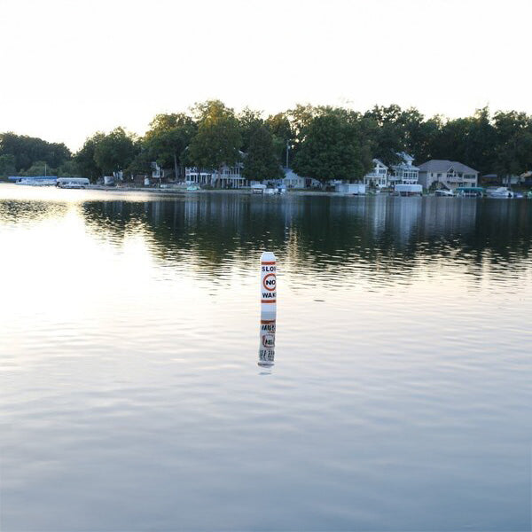 Buoy floating in a calm lake with houses and trees in the background