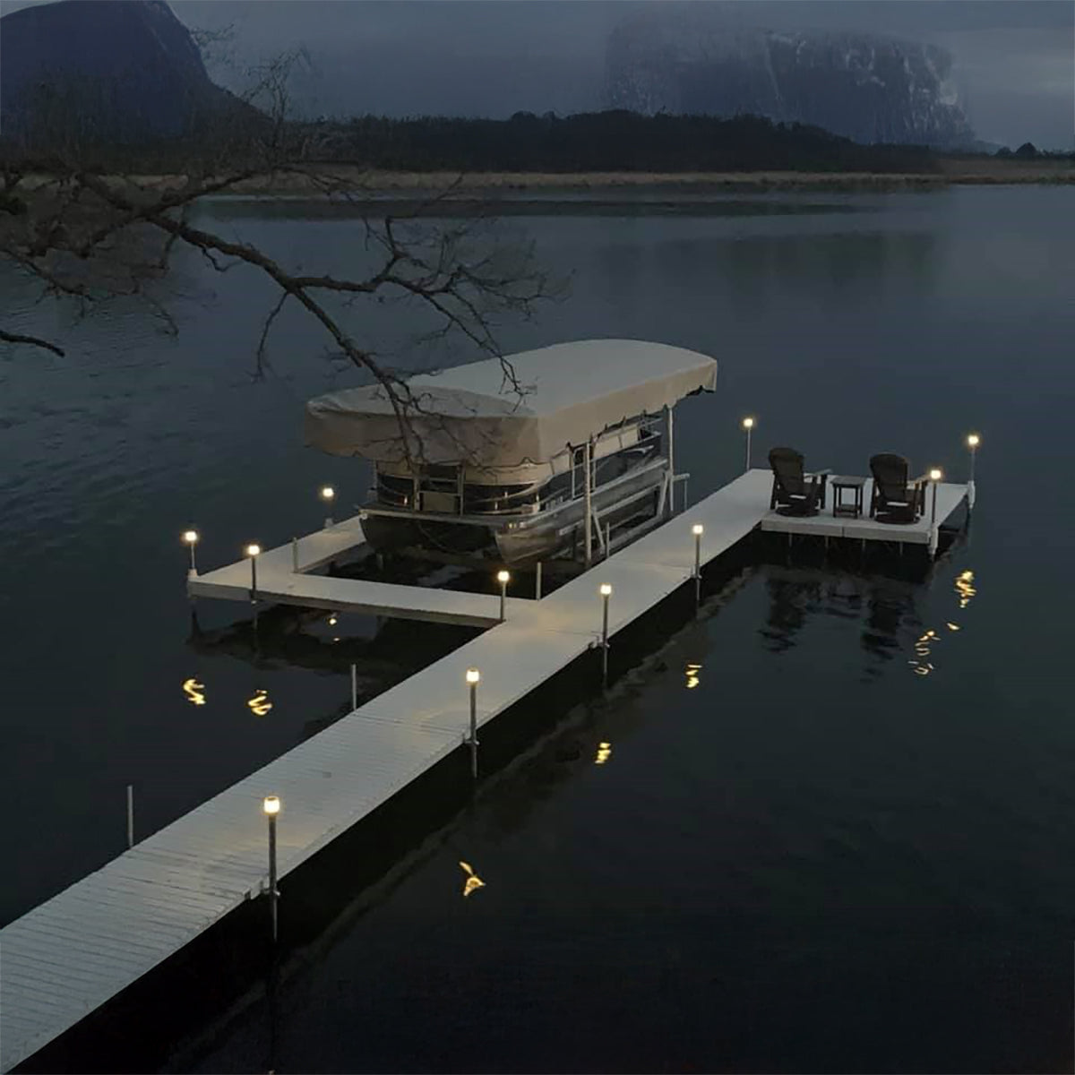 Dock with a covered boat on a lake at night, surrounded by mountains.