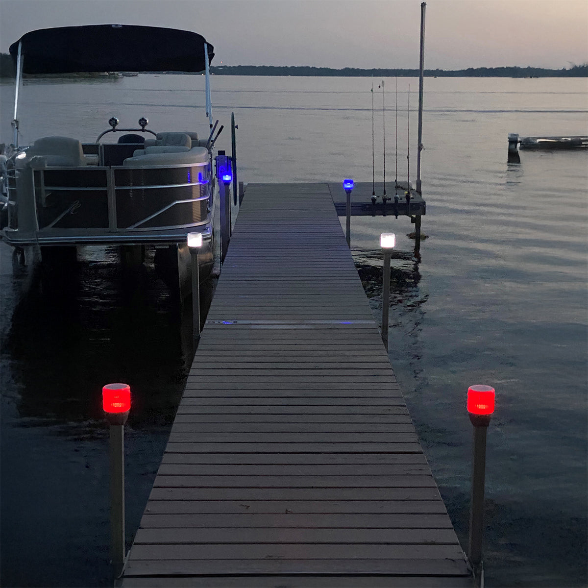 Boat docked at a wooden pier with red lights on a calm lake at dusk.